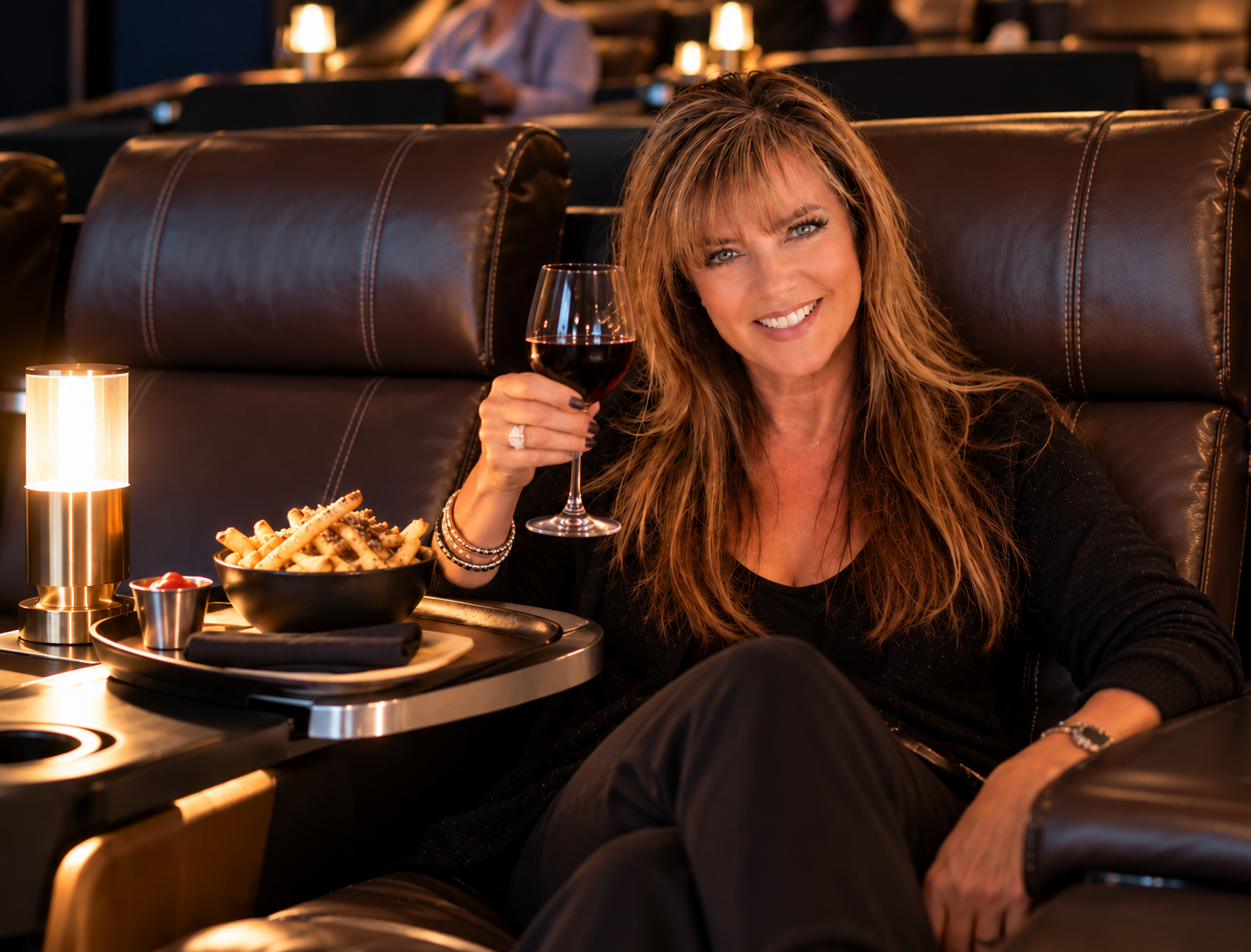 Woman enjoying red wine and fries from a leather recliner at a Cineplex VIP movie theatre.
