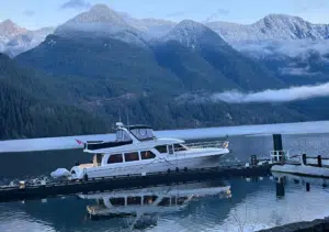Snowy mountains reflect on calm water with a boat at a dock